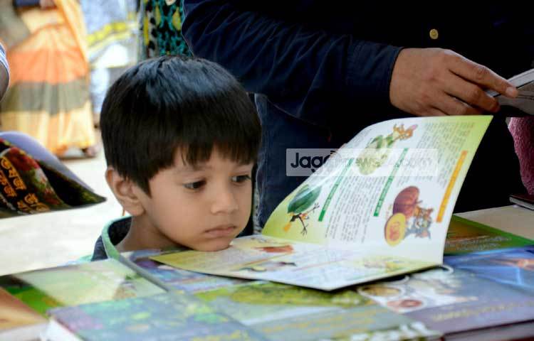 বইমেলায় এসে প্রিয় বইয়ের ভুবনে হারিয়ে গেছে এ শিশু। ছবি : বিপ্লব দিক্ষিৎ