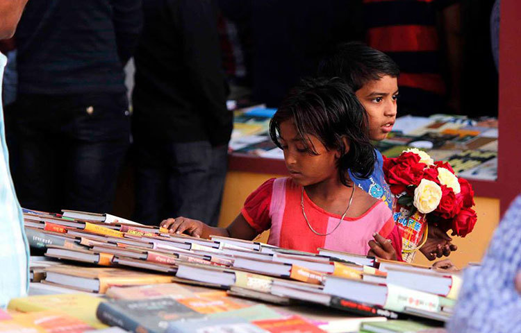 মেলার মাঠে ফুল বিক্রি করতে করতে বই নেড়েচেড়ে দেখছে দুই পথশিশু। ছবি : মাহবুব আলম