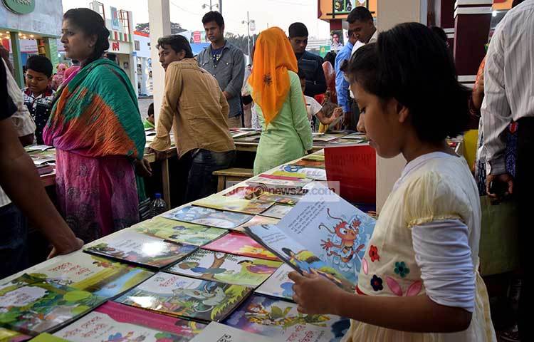 স্টলের চারদিকে পাঠকের ভিড়। শিশুটি তার প্রিয় বইয়ের পাতায় ডুবে আছে। ছবি : মাহবুব আলম