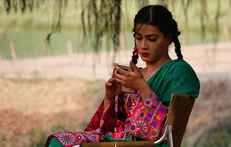 গ্রামের এই মেঠোপথে বসে মোবাইল ফোনে মাহি হয়তো ফেসবুক ব্যবহার করছেন। ছবি : রকিবুল ইসলাম