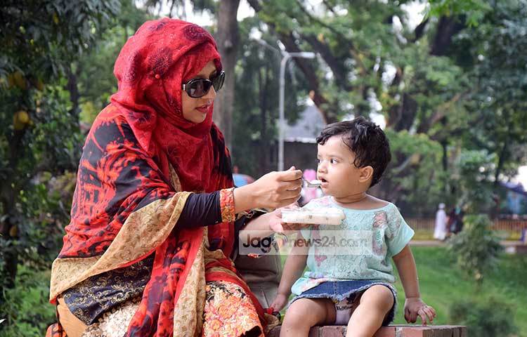 সন্তানকে নিয়ে পার্কে ঘুরতে এসে মমতা মাখা হাতে খাইয়ে দিচ্ছেন একজন মা। ছবি : মাহবুব আলম