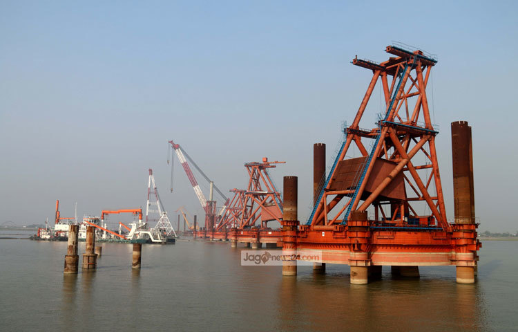 নির্দিষ্ট কর্মপরিকল্পনা অনুযায়ী এগিয়ে চলছে দেশের সর্ববৃহৎ প্রকল্প পদ্মা বহুমুখী সেতুর নির্মাণ কাজ। সেতু নির্মাণে বিশাল কর্মযজ্ঞ চলছে পদ্মা নদীর দুই পাড়ে। ছবি : মাহবুব আলম