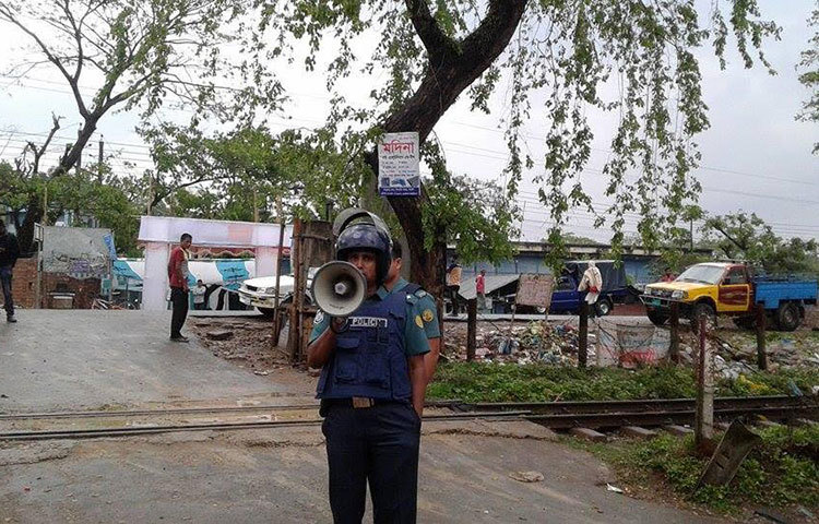 হ্যান্ড মাইক দিয়ে জঙ্গিদের আত্মসমর্পণ করার জন্য আহবান জানাচ্ছেন এক পুলিশ সদস্য।