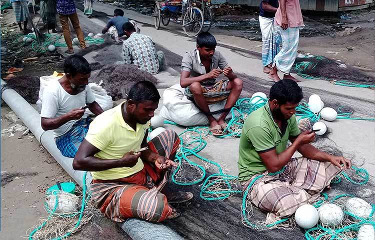 জেলেরা কালো সুতোর পুরনো জালের ছেড়া অংশ বুনে মেরামত করছেন। ছবি : কাজী সাঈদ