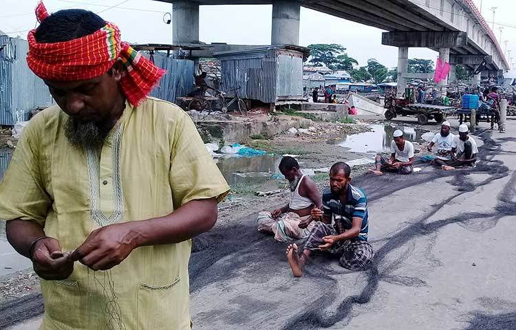 জেলেরা কালো সুতোর পুরনো জালের ছেড়া অংশ বুনছেন। এভাবেই কাটছে জেলেদের সময়। ছবি : কাজী সাঈদ