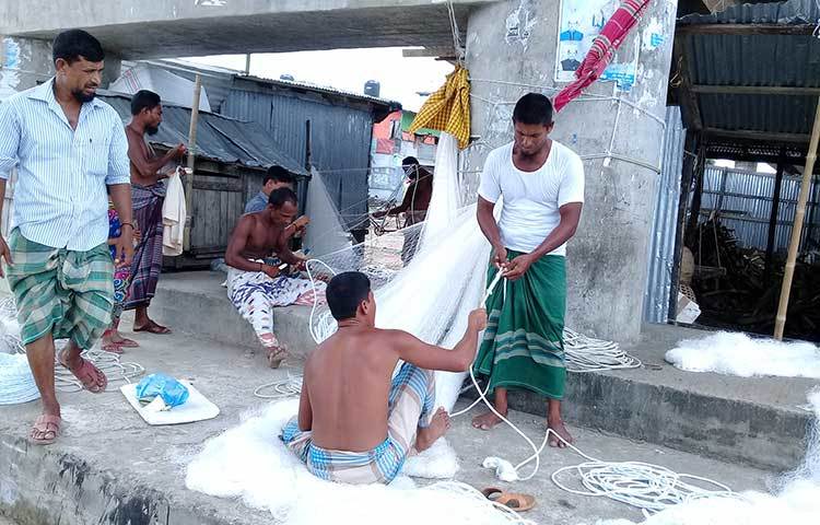 জেলেরা সাদা সুতোর নতুন জালে দড়ি লাগাচ্ছেন। ছবি : কাজী সাঈদ