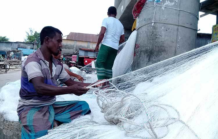 সাদা সুতার নতুন জালে দড়ি লাগাচ্ছেন এক জেলে। ছবি : কাজী সাঈদ