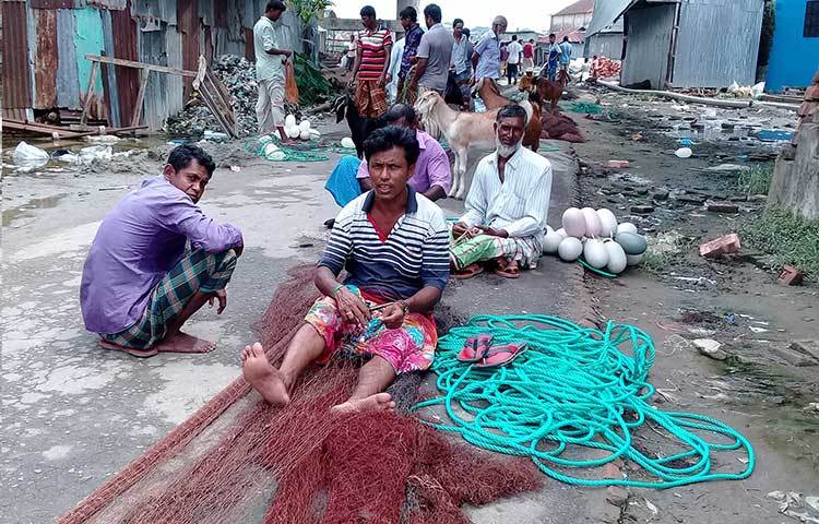 লাল সুতার পুরনো জালের ছিড়া বুনানোর কাজে ব্যস্ত কয়েকজন জেলে। ছবি : কাজী সাঈদ