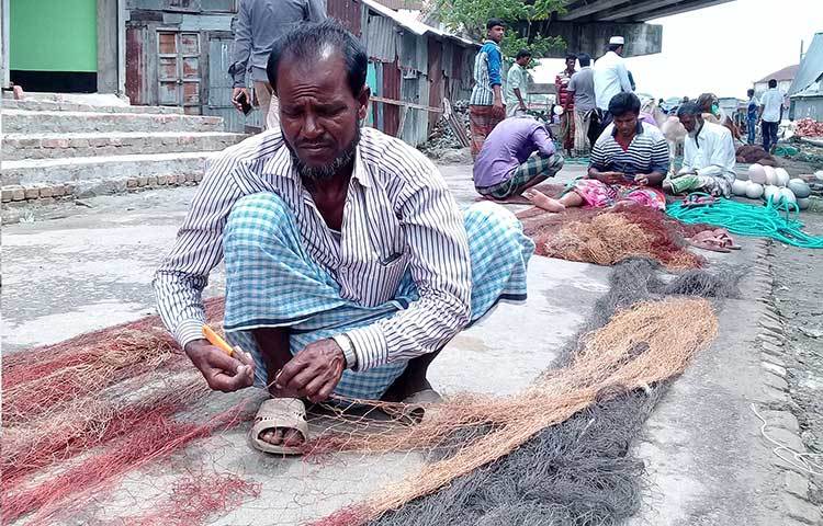 লাল সুতার পুরনো ছেড়া অংশ চাকু দিয়ে কেটে সমান করছেন এক জেলে। ছবি : কাজী সাঈদ