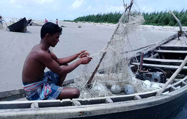 উত্তাল সমুদ্র থেকে গাছের ডাল প্যাঁচানো জাল তুলে এনে ছাড়াচ্ছেন এক জেলে। ছবি : কাজী সাঈদ