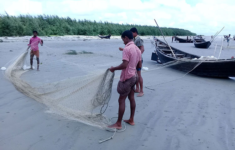 সমুদ্র থেকে তুলে আনা এলোমেলো জাল গোছাচ্ছেন তিন জেলে। ছবি : কাজী সাঈদ