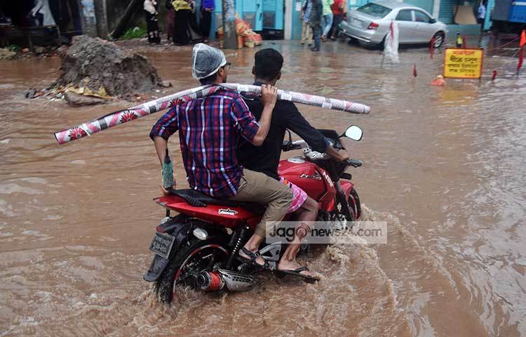 পানির মধ্যে মোটর সাইকেল চালিয়ে যাচ্ছেন কর্মব্যস্ত দুই ব্যক্তি। খানাখন্দে ভরা রাস্তা দিয়ে খুব সতর্কতার সঙ্গে তাদের যেতে হচ্ছে। ছবি : মাহবুব আলম