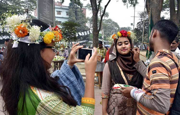 এক তরুণী আরেক তরুণীর গালে বিজয়ের আলপনা আঁকার দৃশ্য ক্যামেরা বন্দি করছেন। ছবি : বিপ্লব দিক্ষিৎ