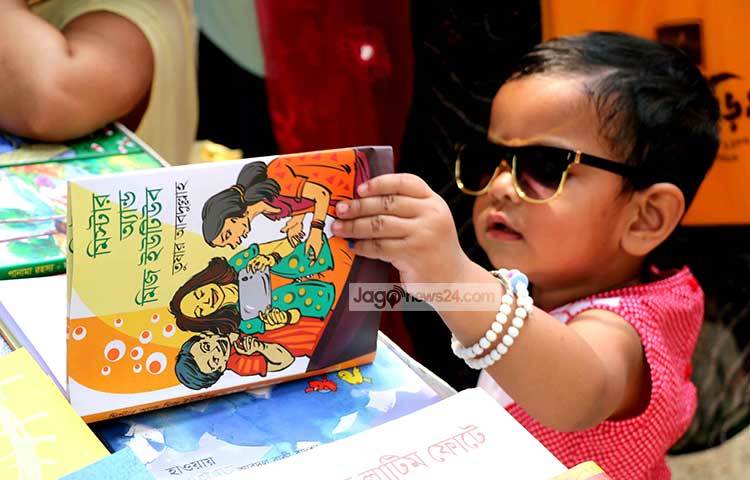 বাবা-মায়ের সঙ্গে মেলায় এসে শিশুটি বই খুলে দেখছে-এর চেয়ে নান্দনিক দৃশ্য আর কী হতে পারে। ছবি : বিপ্লব দিক্ষিৎ