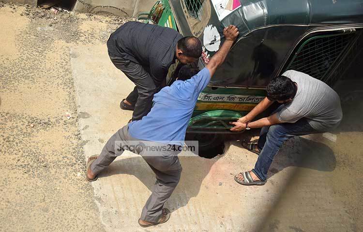 ম্যানহোলের গর্তে পড়েছে সিএনজির চাকা। তিনজন মিলে তোলার চেষ্টা করছেন। সিটি কর্পোরেশনের এই উদাসীনতার কারণে ঘটছে দুর্ঘটনা। ছবি : মাহবুব আলম