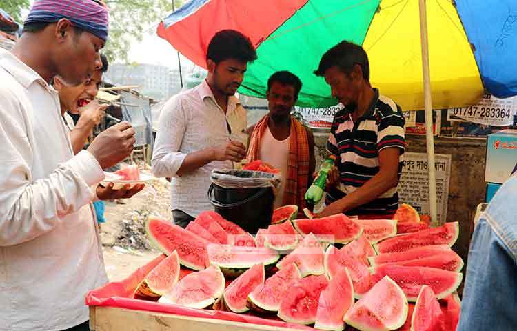 বিক্রির জন্য তরমুজ কেটে রাখা হয়েছে, অন্যদিকে ক্রেতারা কিনে খাচ্ছেন। ছবি : বিপ্লব দিক্ষিৎ
