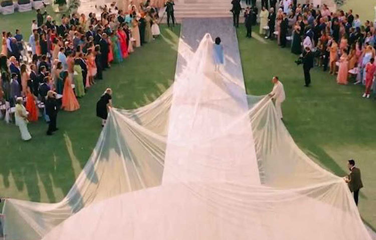 সাদা রঙের লেস বসানো, ফুলহাতা গাউন পরেছিলেন প্রিয়াঙ্কা। তার পিছনে শিফনের সাদা ভেইল বসানো ছিল। কিন্তু সেটা এতটাই লম্বা ছিল যে সামলাতে হাত লাগাতে হয় জনা কয়েক লোকজনকে।