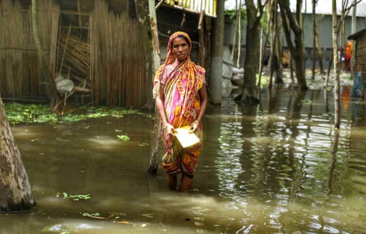 বন্যার্ত মানুষের গলার কাঁটা কিস্তি পরিশোধ করা। এক হাঁটু পানি ভেঙে পাড়ার মধ্যে আসা এনজিওকর্মীদের হাতে তুলে দিতে হচ্ছে টাকা। ছবি: মাহবুব আলম