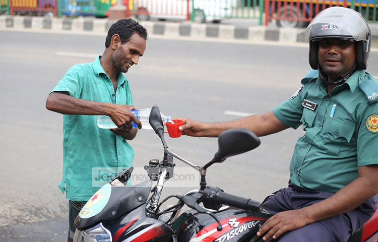 দায়িত্ব পালনরত এক পুলিশ সদস্যকে পানি পান করাচ্ছেন একজন পানি বিক্রেতা। ছবি: মাহবুব আলম