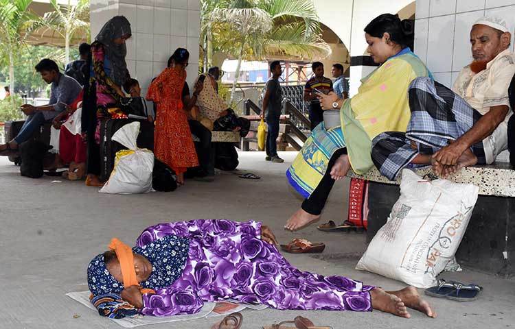 ট্রেনের অপেক্ষায় বসে আছেন যাত্রীরা। অপেক্ষা করতে করতে এক নারী ক্লান্ত হয়ে স্টেশনের মেঝেতেই শুয়ে পড়েছেন। ছবি: বিপ্লব দিক্ষিৎ