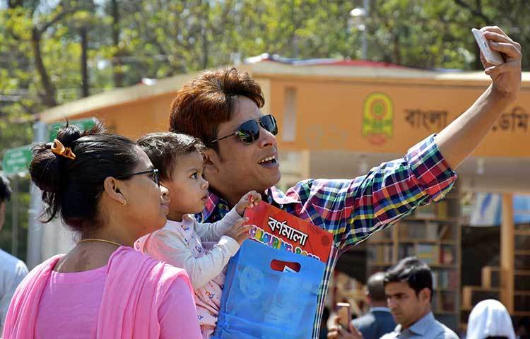 শিশু সন্তানকে মেলায় নিয়ে এসে সেলফি তুলছেন বাবা-মা। ছবি: বিপ্লব দিক্ষিৎ