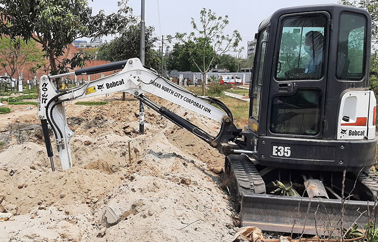 দেশে করোনাভাইরাসে মৃতের সংখ্যা ১০ হাজার ছাড়িয়েছে। এমন পরিস্থিতিতে কর্মব্যস্ততা বেড়েছে ঢাকা উত্তর সিটি করপোরেশনের (ডিএনসিসি) আওতাভুক্ত রায়েরবাজার কবরস্থানের কর্মীদের। মরদেহ সমাহিত করতে খুঁড়তে হচ্ছে নতুন নতুন কবর। ছবি: জাগো নিউজ