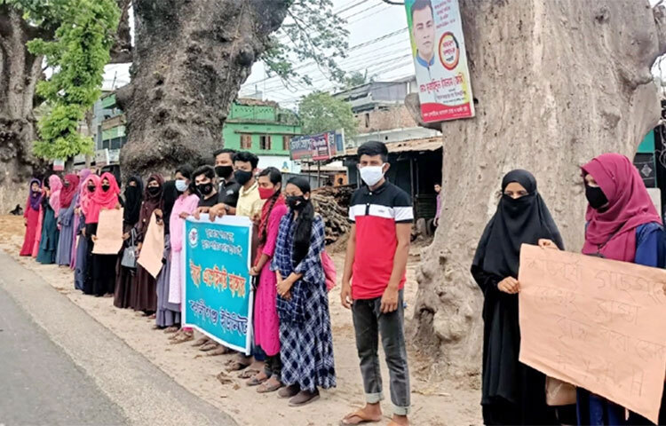সারিবদ্ধ দাঁড়িয়ে থাকা শতবর্ষী রেইনট্রিগুলো রেখেই যশোর-ঝিনাইদহ মহাসড়কের ছয়লেন নির্মাণের দাবিতে মানববন্ধন করেছে স্বেচ্ছাসেবী সংগঠন ইয়ুথ এগেইনস্ট হাঙ্গার। আজ বেলা ১১টার দিকে ঝিনাইদহের কালীগঞ্জ পৌরসভায় বৈশাখী তেল পাম্প এলাকায় এ মানববন্ধন অনুষ্ঠিত হয়। এ সময় অনেকের হাতে বিভিন্ন লেখা সংবলিত প্ল্যা-কার্ড দেখা যায়। ছবি: আব্দুল্লাহ আল মাসুদ