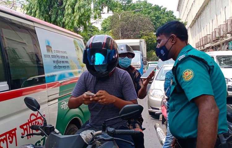 এই মটোরসাইকেল আরোহীকে লকডাউনের মধ্যে বাইরে বের হওয়ার কারণ জানতে চাইছেন পুলিশ সদস্য। ছবি: জাগো নিউজ