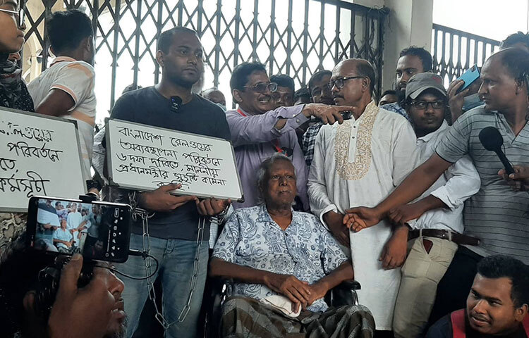 ডা. জাফরুল্লাহ চৌধুরীকেও ঢুকতে দেওয়া হয়নি কমলাপুর রেলওয়ে স্টেশনের ভেতরে। স্টেশনে প্রবেশের জন্য বারবার নিরাপত্তা বাহিনীর প্রতি অনুরোধ জানান গণস্বাস্থ্য কেন্দ্রের প্রতিষ্ঠাতা। পরে তিনি ভেতরে প্রবেশ করতে না দেওয়া পর্যন্ত স্টেশনের বাইরে অবস্থান নিয়ে থাকার ঘোষণা দেন। আজ বিকেল সোয়া ৫টার দিকে মহিউদ্দিন রনিকে নিয়ে ডা. জাফরুল্লাহ কমলাপুর রেলওয়ে স্টেশন ম্যানেজারের সঙ্গে দেখা করার জন্য হুইল চেয়ারে বসে যেতে চাইলে তাকে বাধা দেওয়া হয়। ছবি: বিপ্লব দিক্ষিৎ