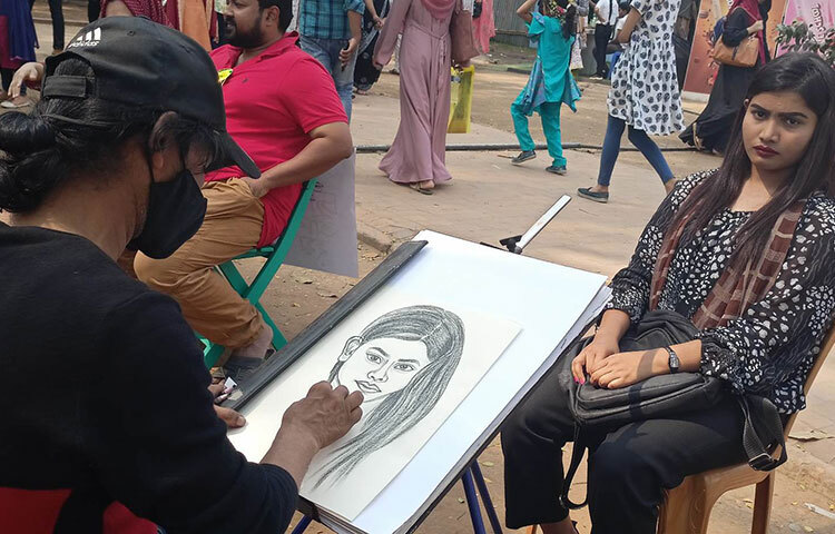 বইমেলায় আসা শিল্প-সাহিত্যপ্রেমীদের অনেকেই চিত্রকর্মের ভক্ত। অনেকে প্রিয়জন-স্বজনের ছবি এঁকেও বাঁধিয়ে রাখতে চান। বইমেলায় চিত্রশিল্পীরা সেসব মানুষের আনন্দটা আরও বাড়িয়ে দিচ্ছেন। এতে শিল্পীদের আয়ও ভালো। ছবি: জাগো নিউজ