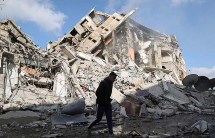 ইসরায়েলি বিমান বাহিনীর হামলায় ধ্বংসস্তূপে পরিণত একটি বহুতল ভবন, পাশ দিয়ে হেঁটে যাচ্ছেন এক ফিলিস্তিনি। ছবি: রয়টার্স