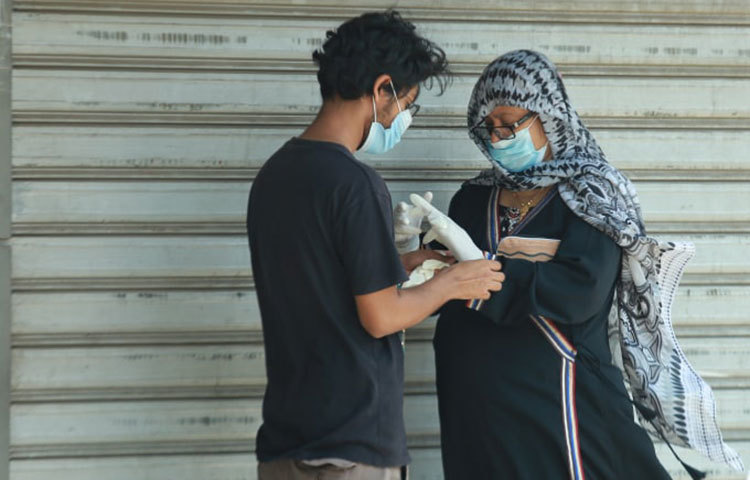জরুরি কাজে বের হওয়া এই নারীকে হ্যান্ড গ্লোভস পরিয়ে দেয়া হচ্ছে। ছবি: মাহবুব আলম