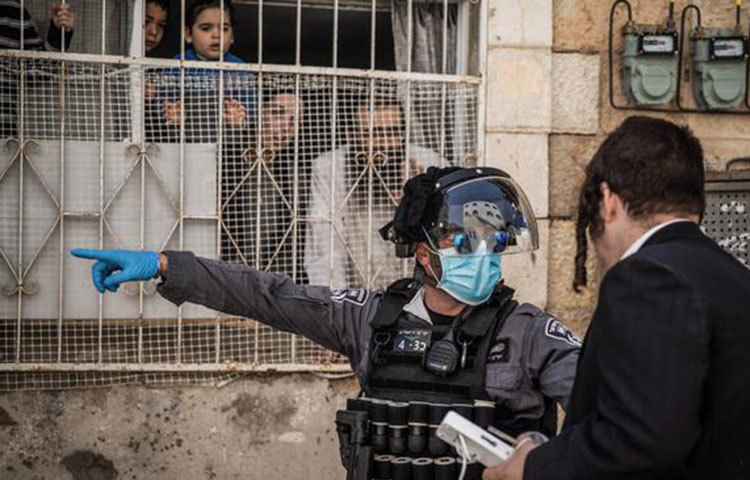 দেশটিতে কারফিউ জারি করা হয়েছে। কট্টর ইহুদিরাও কঠোর নিয়ম মানতে বাধ্য হচ্ছেন। ছবিতে মাস্ক পরা এক পুলিশ কর্মকর্তাকে একজন চরম কট্টর ব্যক্তিকে ঘরে ফিরে যাওয়ার নির্দেশ দিতে দেখা যাচ্ছে।