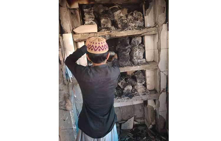 আগুনে পুড়ে ছাই হওয়া ধর্মীয় বইপত্র দেখছে একটি শিশু।