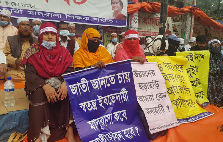 বঙ্গবন্ধুর জন্মশতবার্ষিকীতে দেশের সব ইবতেদায়ি মাদরাসা জাতীয়করণসহ সাত-দফা দাবি আদায়ের লক্ষ্যে অবস্থান ধর্মঘট পালন করছে বাংলাদেশ স্বতন্ত্র ইবতেদায়ি মাদরাসা শিক্ষক সমিতি। শনিবার (২১ নভেম্বর) জাতীয় প্রেস ক্লাবের সামনে সপ্তম দিনের মতো অবস্থান কর্মসূচি পালন করছেন মাদরাসা শিক্ষকরা।