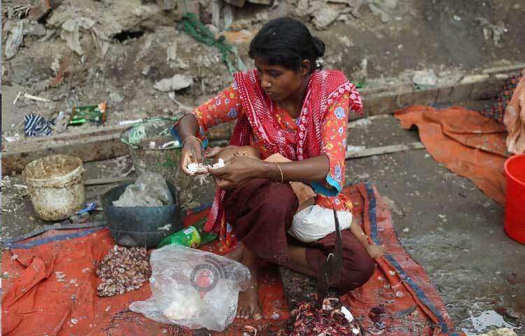 ছোট্ট শিশুকে কোলে নিয়েই জীবিকার তাগিদে মাছ কাটছেন বৃষ্টি মনি নামের এক নারী। ছবি: মাহবুব আলম