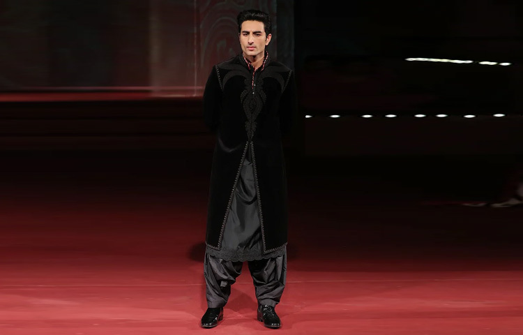 অন্যদিকে, ইব্রাহিম যেন হুবহু সাইফ আলী খানের তরুণ প্রতিচ্ছবি। তার পরনে ছিল ঘন কালো রঙের সূক্ষ্ম কারুকাজে মোড়া শেরওয়ানি, যার ওপরের পাইপিং আর নকশায় ছিল রাজকীয় ছাপ। ভেতরে পরেছিলেন আফগান প্রভাবযুক্ত সুরমা রঙের সিল্ক কুর্তা-পাজামা। সঙ্গে ছিল কালো ক্লাসিক জুতা।