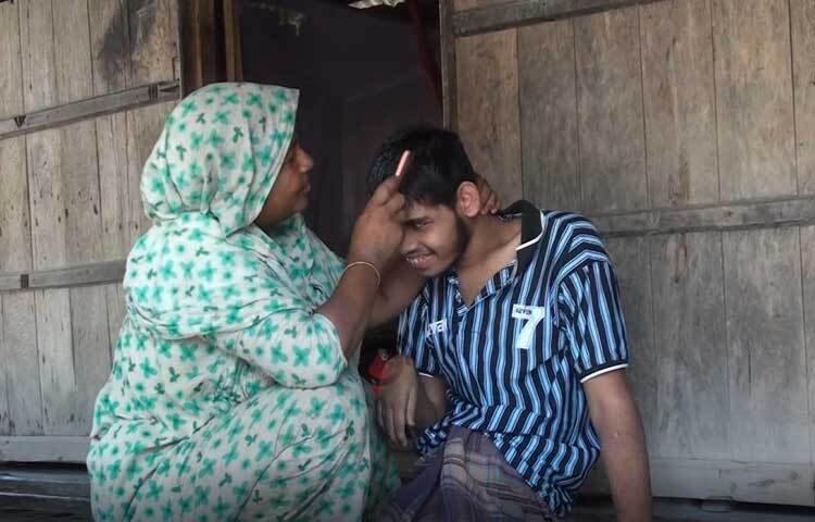 বিশেষ চাহিদাসম্পন্ন ছেলের যত্নে ব্যস্ত মা সুফিয়া বেগম। সাতক্ষীরার শ্যামনগর উপজেলার মুন্সিগঞ্জের সুন্দরবন সংলগ্ন মালঞ্চ নদীর তীরে বেড়িবাঁধের পাশে বাস করেন তারা। ছবি: আহসানুর রহমান রাজীব