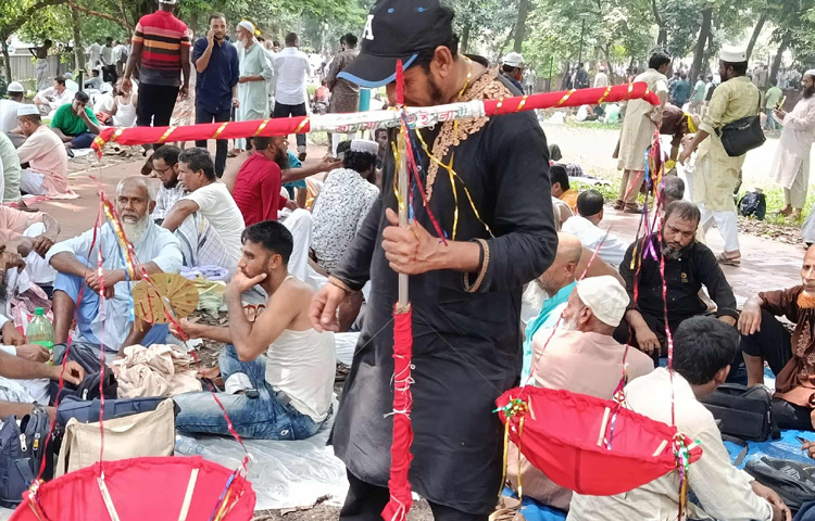 কেউ গাছের ছায়ায় বসে রয়েছেন, কেউ ঘাসে পা ছড়িয়ে শুয়ে আছেন, আবার কেউ ছোট ছোট দলে দলবেঁধে আলোচনা করছেন সামনের পরিকল্পনা নিয়ে। ব্যাগ, পানির বোতল, পোস্টার ও দলীয় পতাকা সঙ্গে নিয়েই এই অবস্থান।