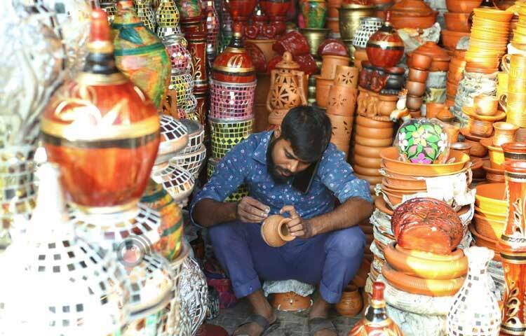 মাঠির তৈরি ছোট কলসে রঙ করতে ব্যস্ত দোকানি।