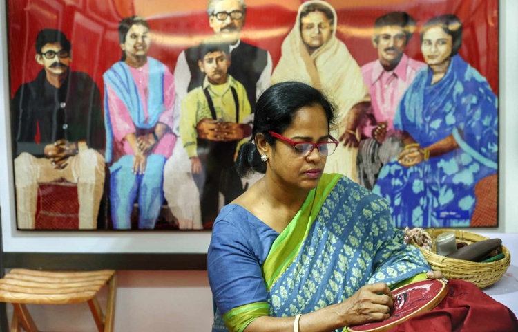 মেলায় নিজ দোকানে বসে সেলাইয়ে ব্যস্ত এক নারী। ছবি: মাহবুব আলম