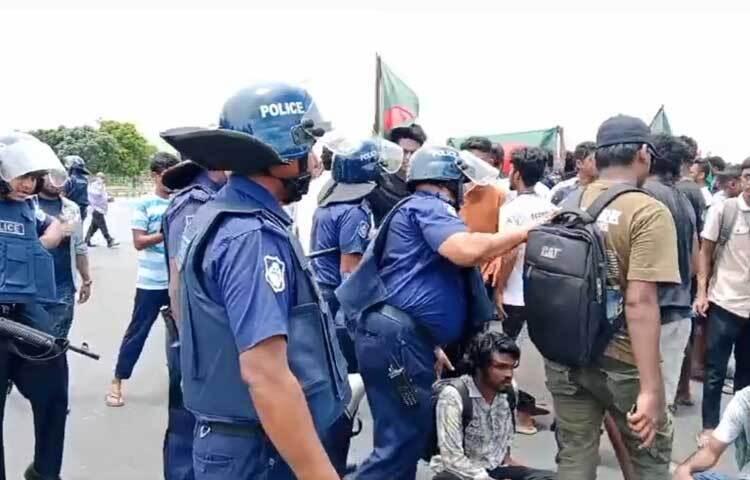 পুলিশ সূত্রে জানা যায়, সকাল সাড়ে ১০টার দিকে পদ্মা সেতু উত্তর থানার সামনে যান চলাচল বন্ধ করে বসে পড়েন দুইশতাধিক শিক্ষার্থী। এসময় পুলিশ তাদের সরিয়ে দেওয়ার চেষ্টা করলে বাকবিতণ্ডা ও ধস্তাধস্তি হয়। এসময় পুলিশ আন্দোলনরত দুই শিক্ষার্থীকে আটক করে। ছবি: আরাফাত রায়হান সাকিব