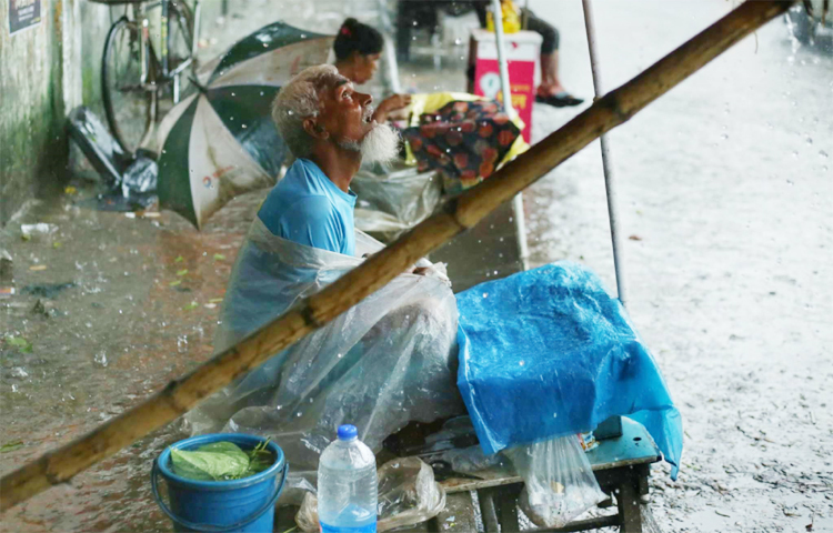 ফুটপাতে তার অস্থায়ী চা, পান, সিগারেটের দোকান। শরীর ও মালামালে পলিথিন জড়িয়ে টানা বৃষ্টিতেও বসে আছেন তিনি ক্রেতার আশায়। মাঝে মাঝে আকাশের দিকেও তাকান। ছবি: মাহবুব আলম