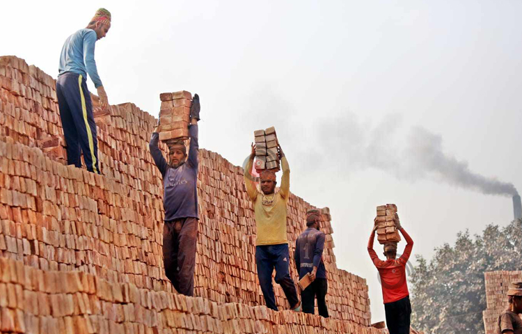 শ্রমিকরা মাথায় করে ইট এক জায়গা থেকে অন্য জায়গায় নিয়ে যাচ্ছে। ছবি: বিপ্লব দীক্ষিত