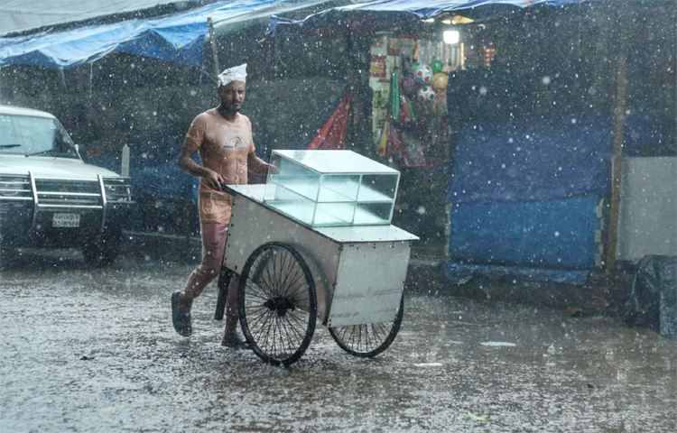 মাথায় পলিথিন পেঁচিয়ে দুই চাকার ভ্রাম্যমাণ দোকান নিয়ে ছুটছেন তিনি। শহরজুড়ে অতিবৃষ্টিতেও তার বিশ্রাম নেই। এতেই নিহীত আছে তার জীবিকা। ছবি: মাহবুব আলম