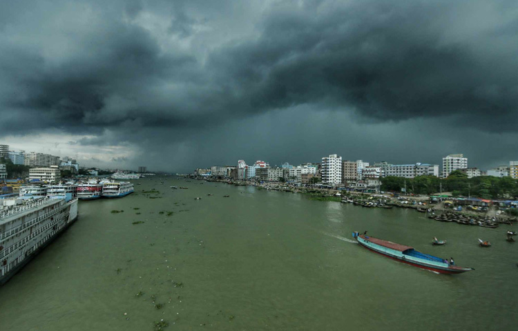 বাবুবাজার ব্রিজ থেকে তোলা ছবিতে ধরা পড়েছে এই বদলে যাওয়া শহরের রূপ। ব্রিজের ওপরে দাঁড়িয়ে দেখা যাচ্ছে একদিকে ঘোলা পদ্মার বুক জুড়ে ছুটে চলা ঢেউ, আর অন্যদিকে কালো মেঘে ঢাকা আকাশ থেকে ঝরছে ঝুম বৃষ্টি। বৃষ্টির সেই ছোঁয়ায় যেন ধুয়ে যাচ্ছে রাস্তাঘাট, মানুষের ক্লান্ত মন আর গরমের যন্ত্রণা।