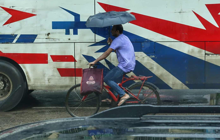 রাস্তায় ভিজে টানটান তারপিচ, বৃষ্টির ফোঁটা গড়িয়ে পড়ছে দোকানের শেড থেকে, পথের ধারের গাছগুলোতেও নতুন প্রাণের ছোঁয়া। অথচ এর মাঝেই জীবনের তাড়না থেমে থাকেনি; কেউ ভিজে গেছে বাসের অপেক্ষায়, কেউ বা পা বাড়িয়েছে ভেজা ফুটপাথে, হাতে শক্ত করে ধরা রঙিন ছাতা।