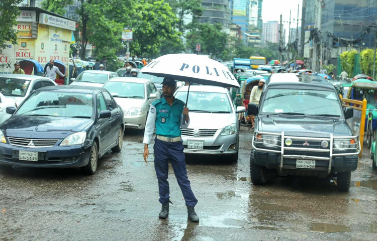 বৃষ্টির মধ্যে ছাতা মাথায় ট্রাফিক সামলাচ্ছেন এক পুলিশ সদস্য।