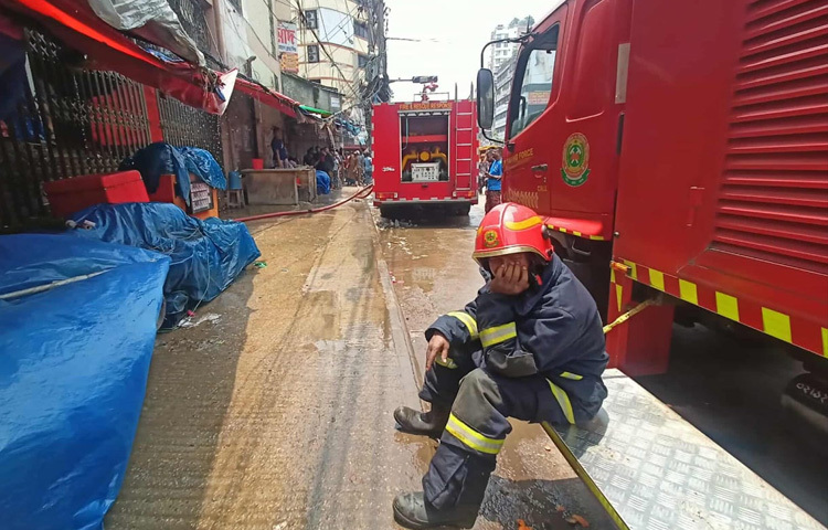 আগুন নেভানোর পর বসে আছেন ক্লান্ত ফায়ার সার্ভিসের কর্মীরা।