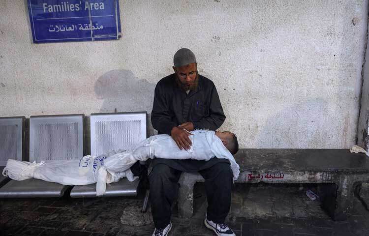 সন্তানের নিথর দেহ নিয়ে বসে আছেন বাবা। ছবি: এএফপি